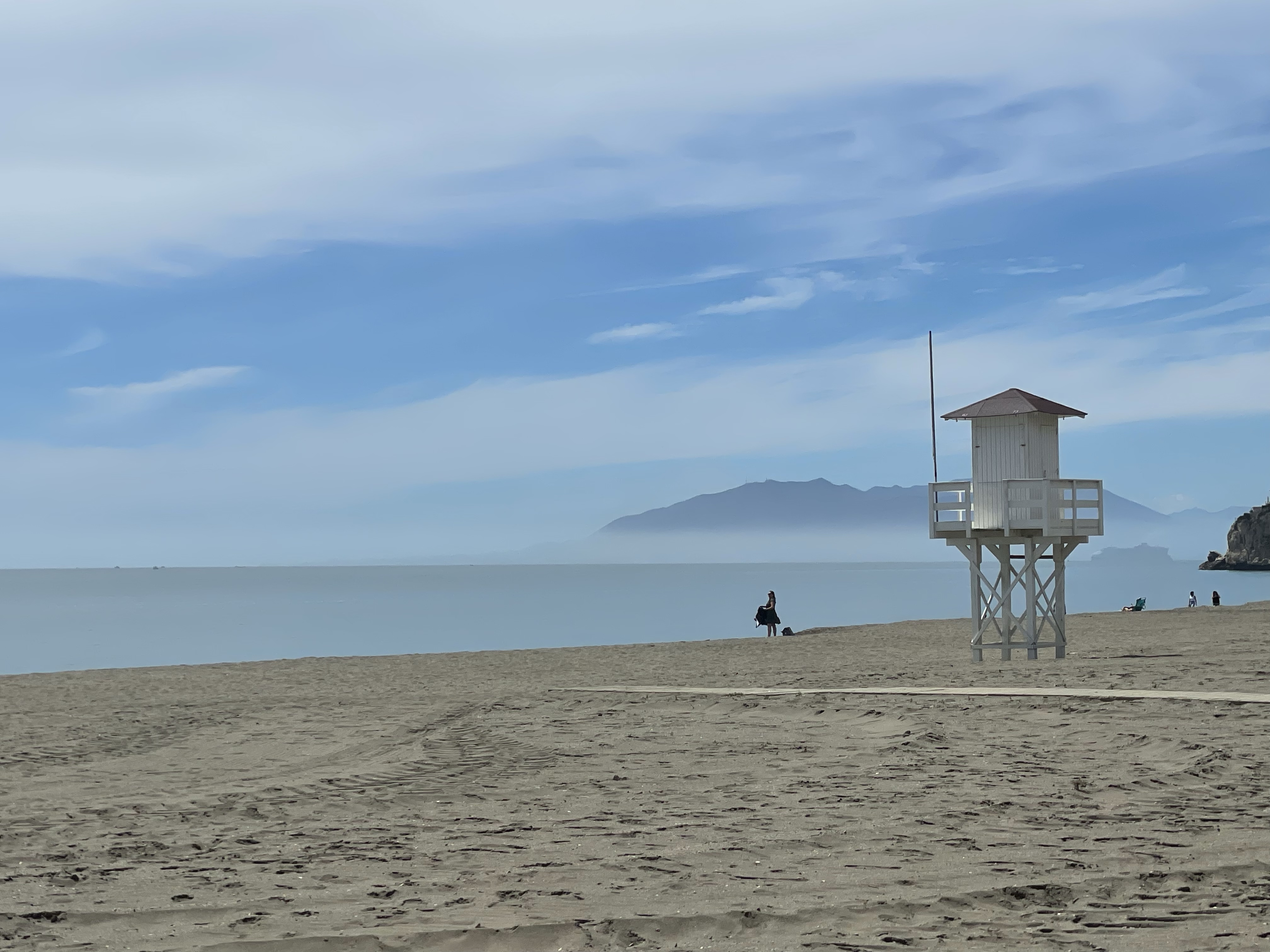 A lifeguard tower on a sandy beach with calm waters and distant mountains under a blue sky.