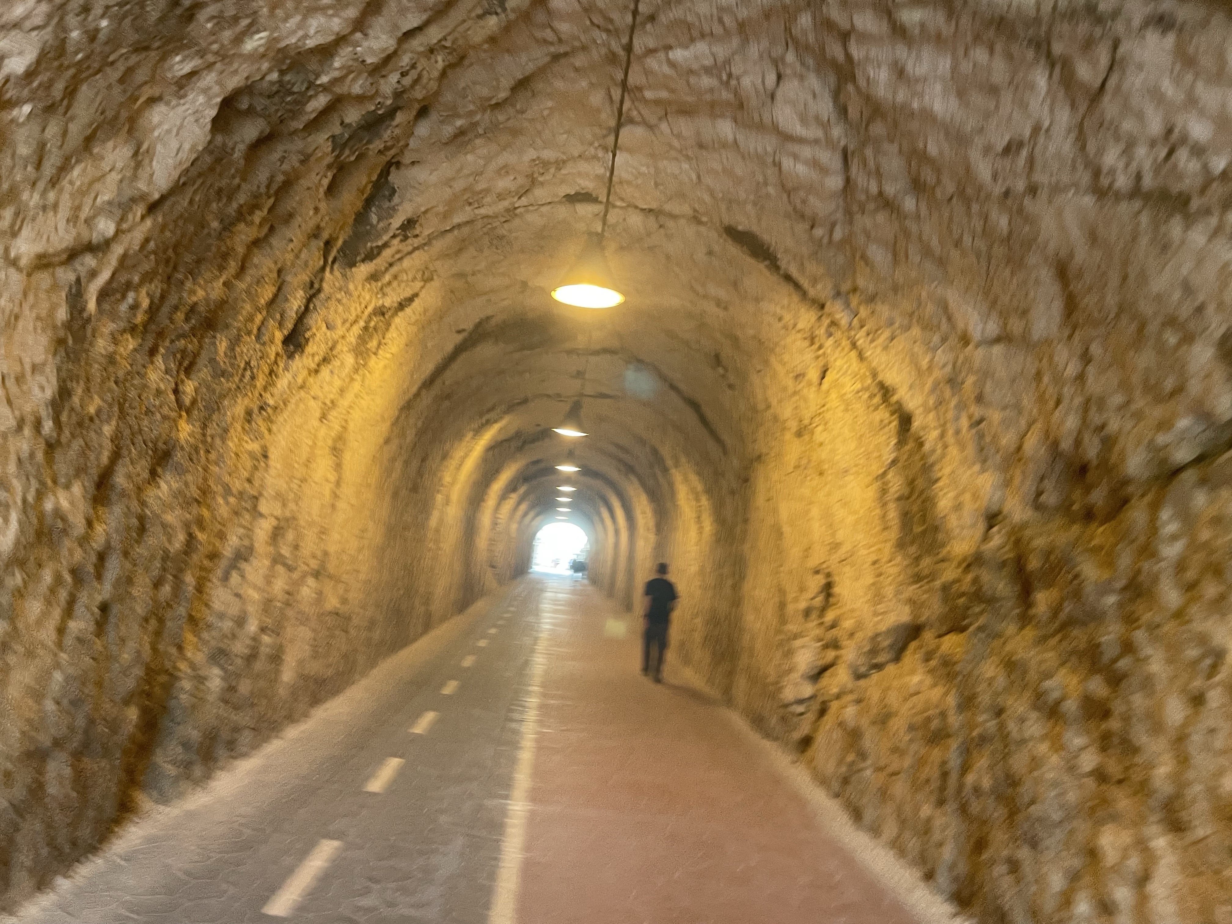 A person walking through a tunnel with rocky walls and overhead lights, creating a warm atmosphere.