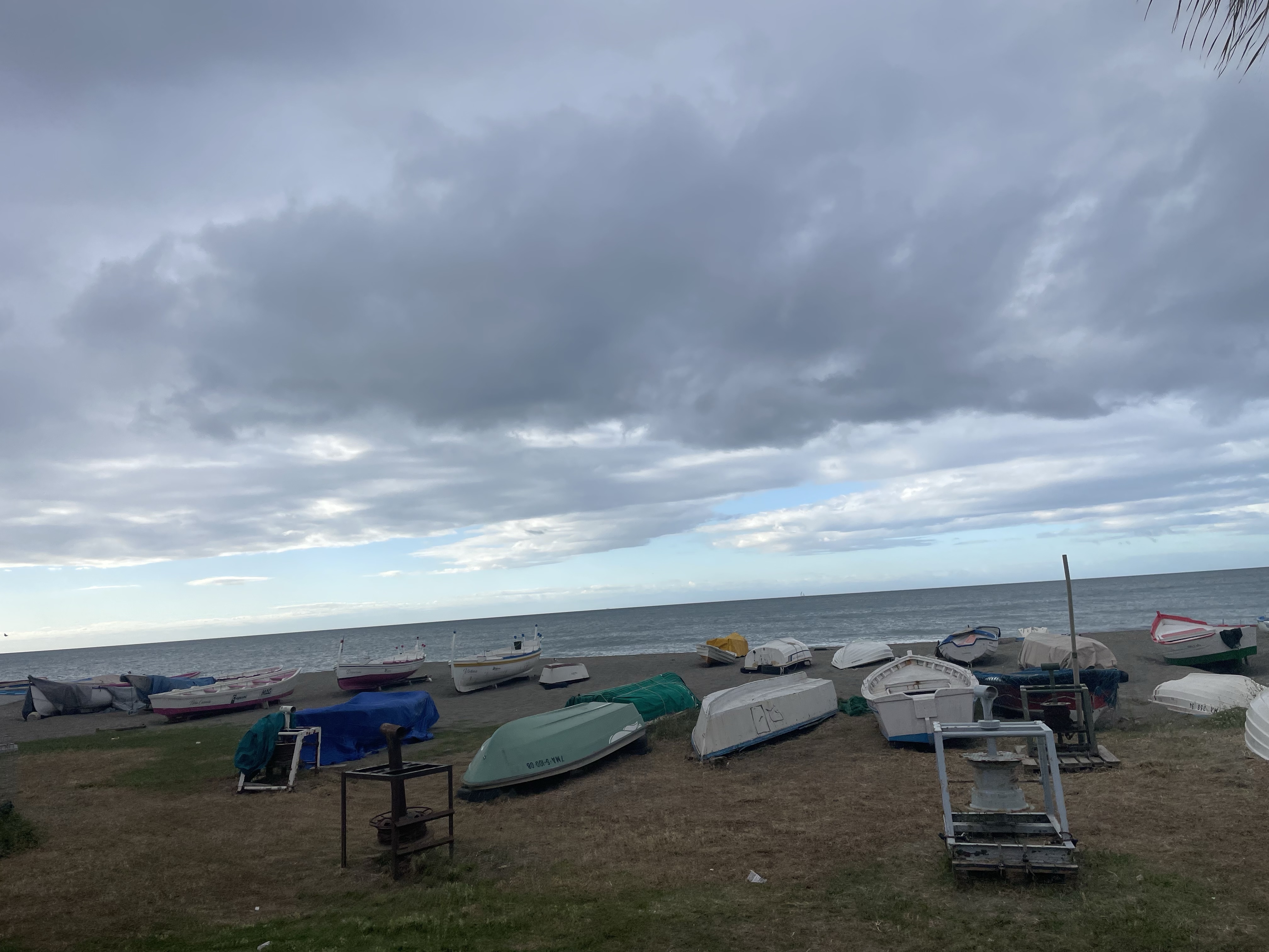 A view of a beach with several boats on the shore under a cloudy sky.